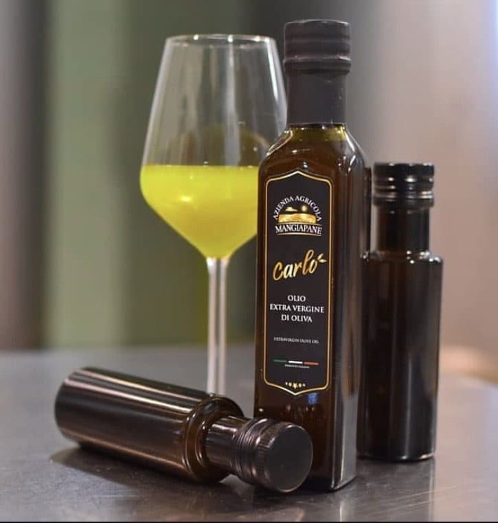 Bottiglie di Olio Carlo extravergine di oliva con un calice di olio appena prodotto